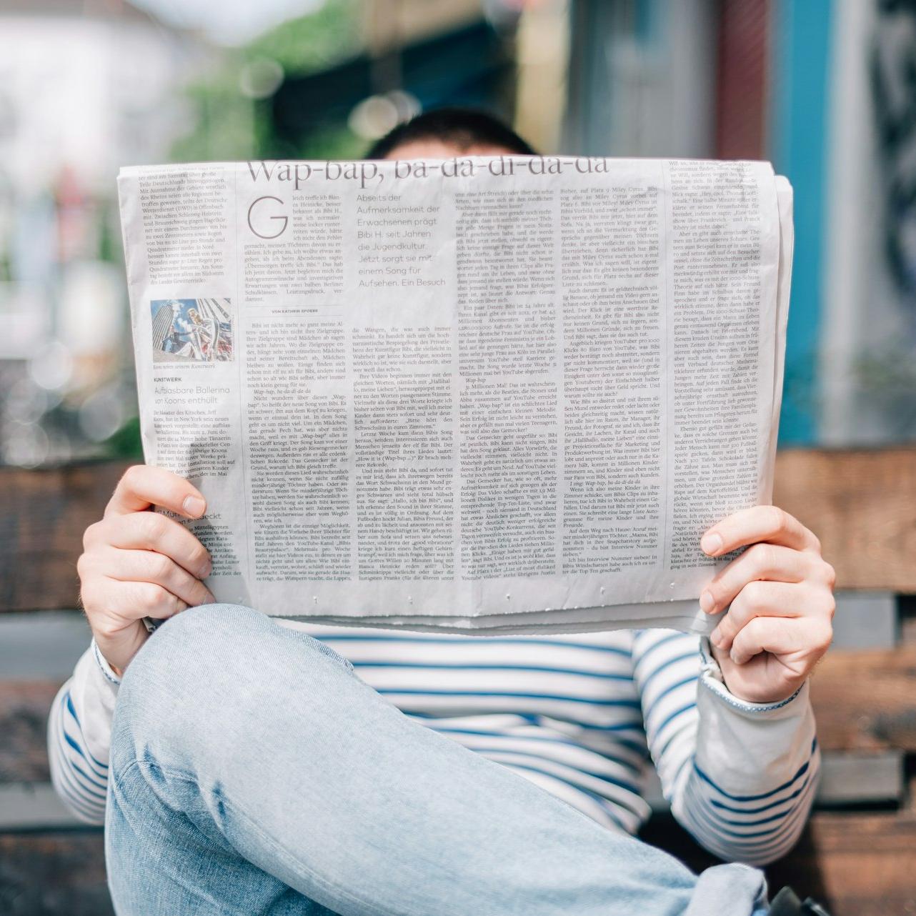 man sitting on bench reading newspaper